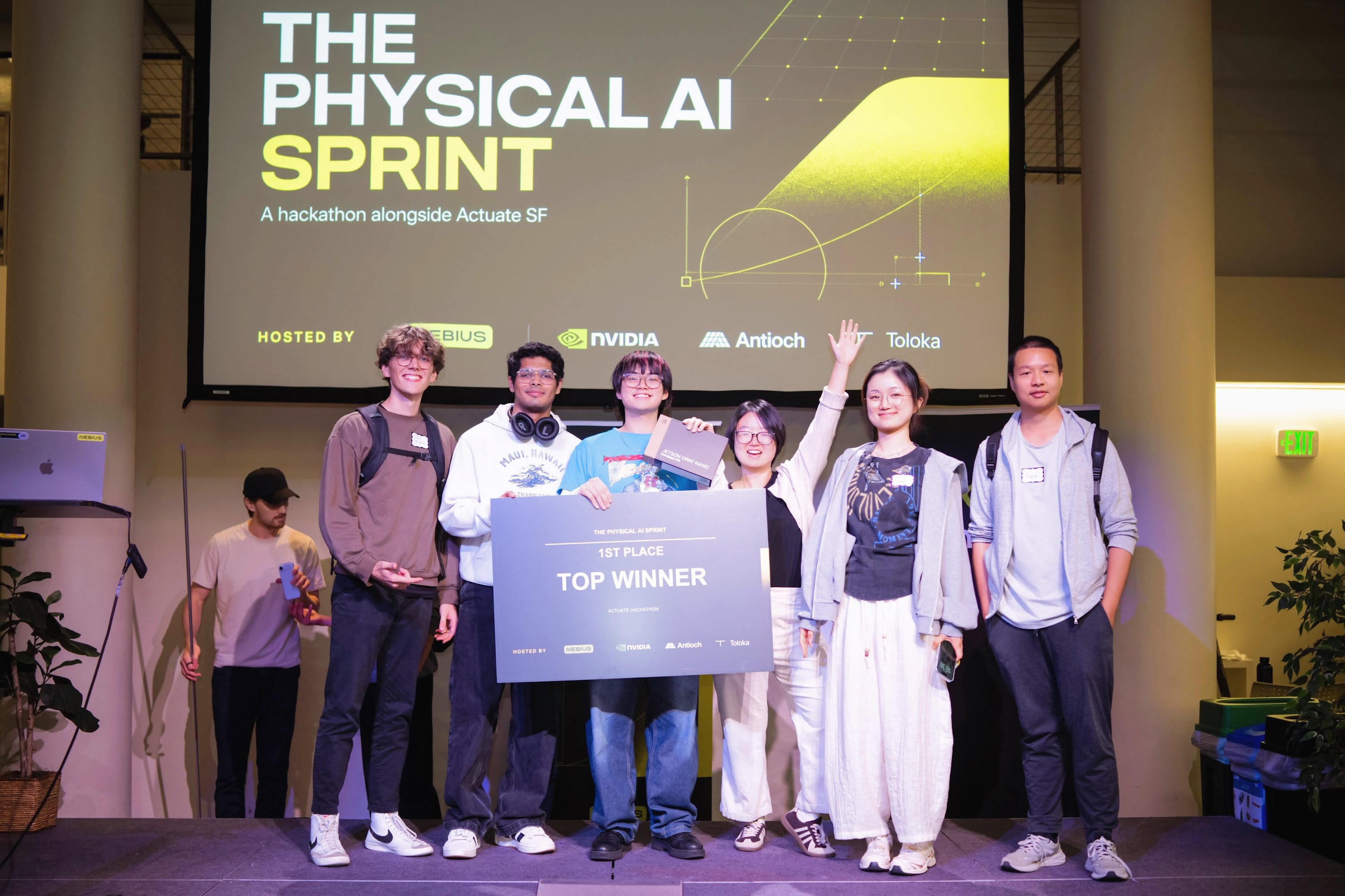 Physical AI Sprint team on stage holding the first-place award beneath the event and sponsor banner